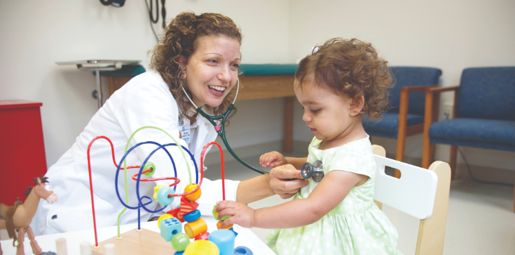 Pediatrician listening to a child's heart with a stethoscope while sitting at a table with toys.